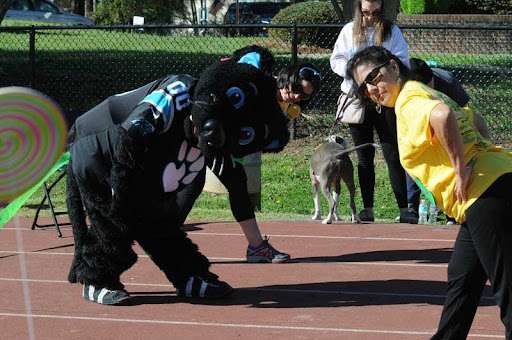 People stretching outdoors with a black panther mascot during a community fitness event.