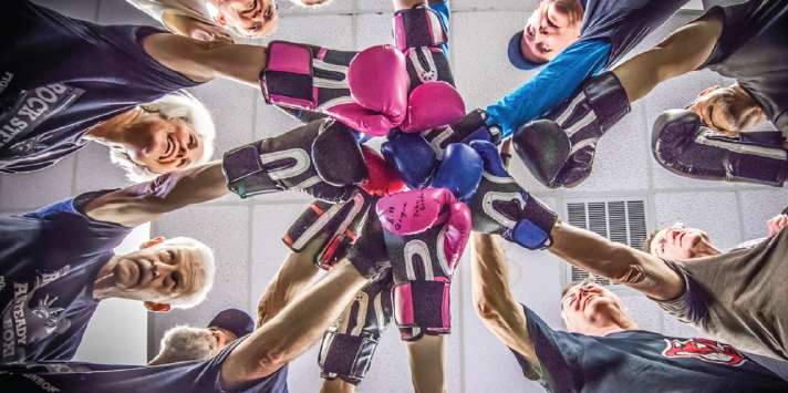 Group of seniors in a boxing circle raising gloved fists, promoting fitness and daily movement for Parkinson’s.