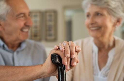 Smiling senior couple with woman’s hand resting supportively over man’s hand on a black cane, symbolizing caregiving and support.