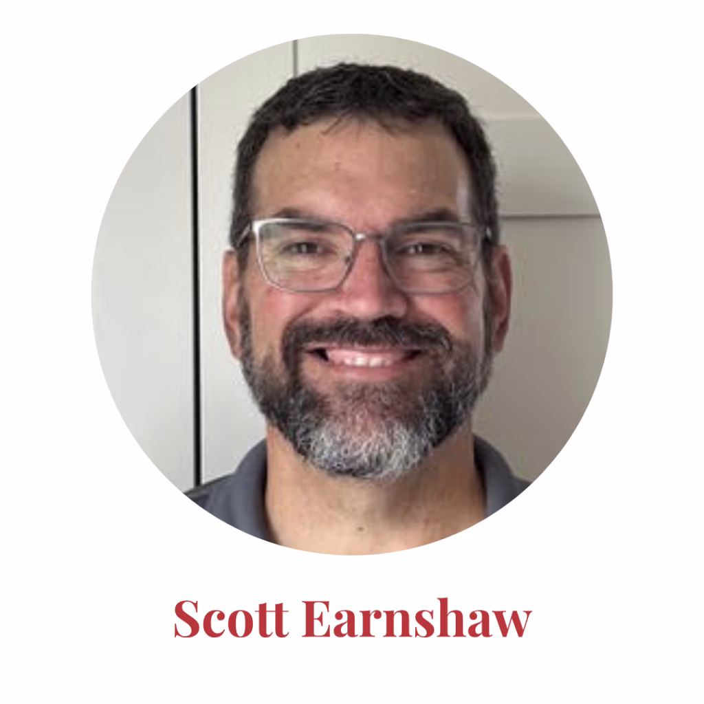 A man with short dark hair, glasses, and a beard smiles at the camera. He is wearing a gray shirt. The text below reads Scott Earnshaw in red.