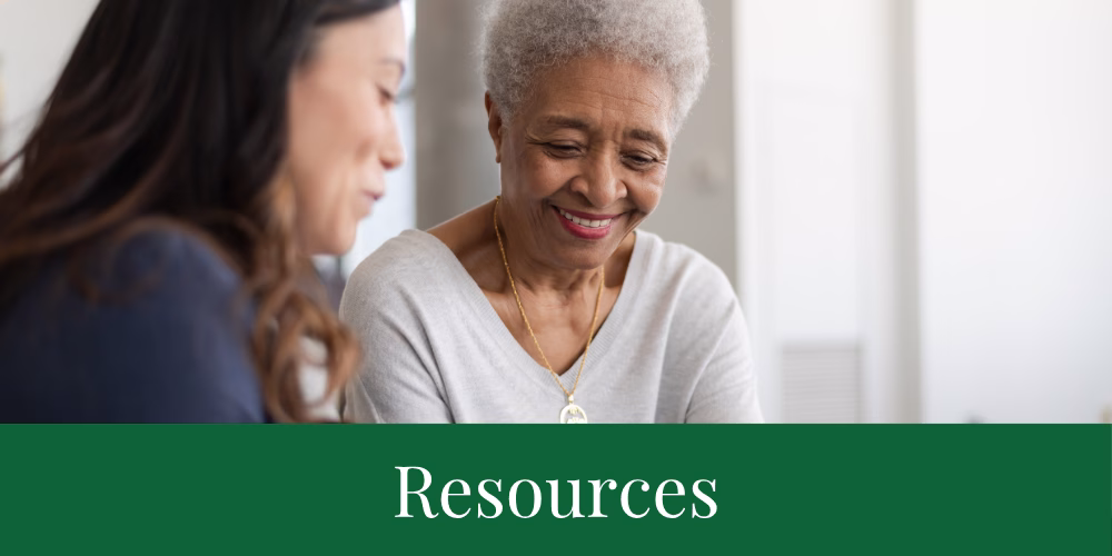 Two women, one older and one younger, sit together and smile as they look at something out of frame. The word Resources is displayed at the bottom on a green background.