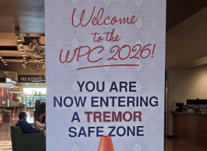 A sign reads: Welcome to the WPC 2026! You are now entering a tremor safe zone, with a cartoon raccoon peeking from behind an orange traffic cone. The hashtag #WPC2026 is at the bottom.